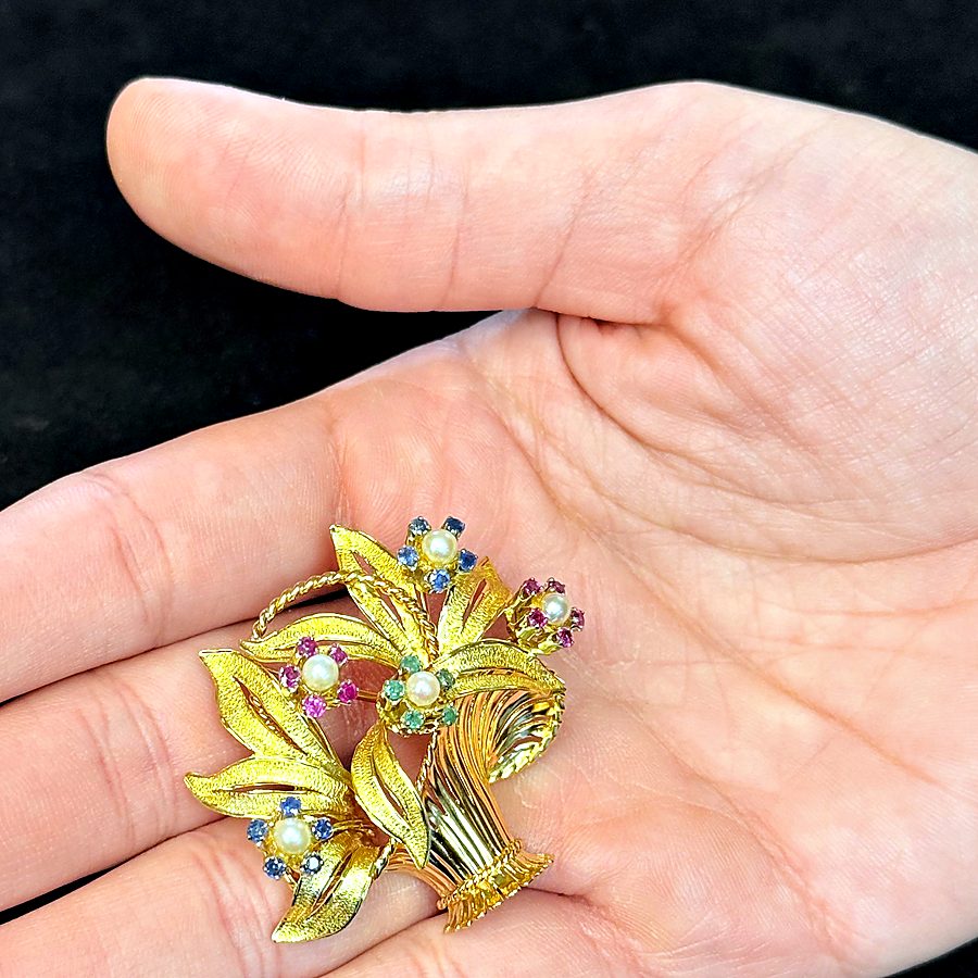 Eine Goldbrosche mit Perlen und farbigen Steinen in der Hand
