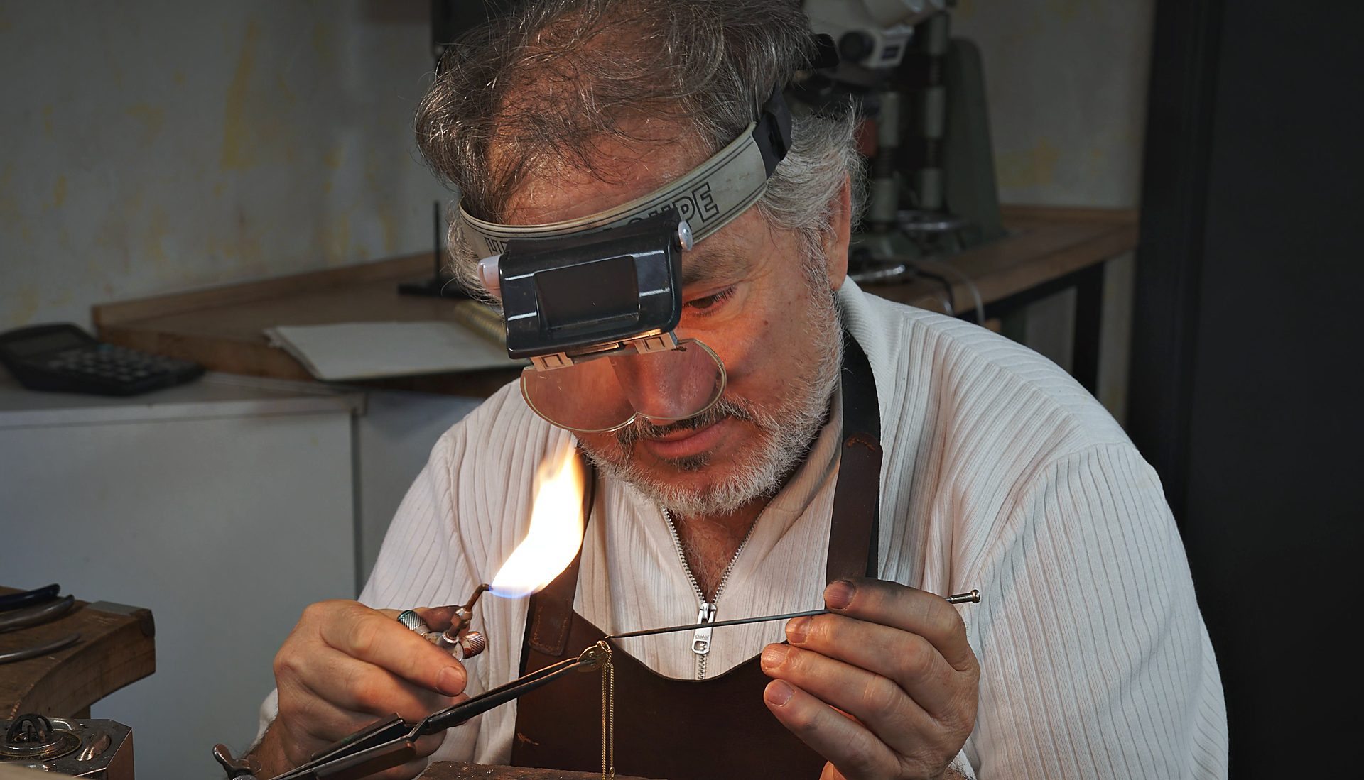 Goldschmied Kamil Akdogan lötet mit Kopflupe und Flamme an der Werkbank